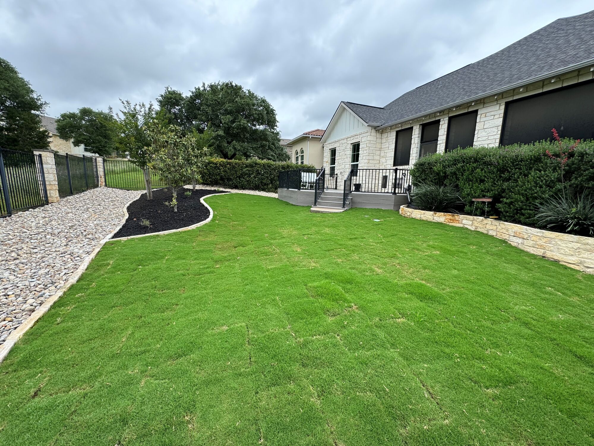 A Pioneer install after establishment: full sod lawn with limestone raised beds and a river rock border