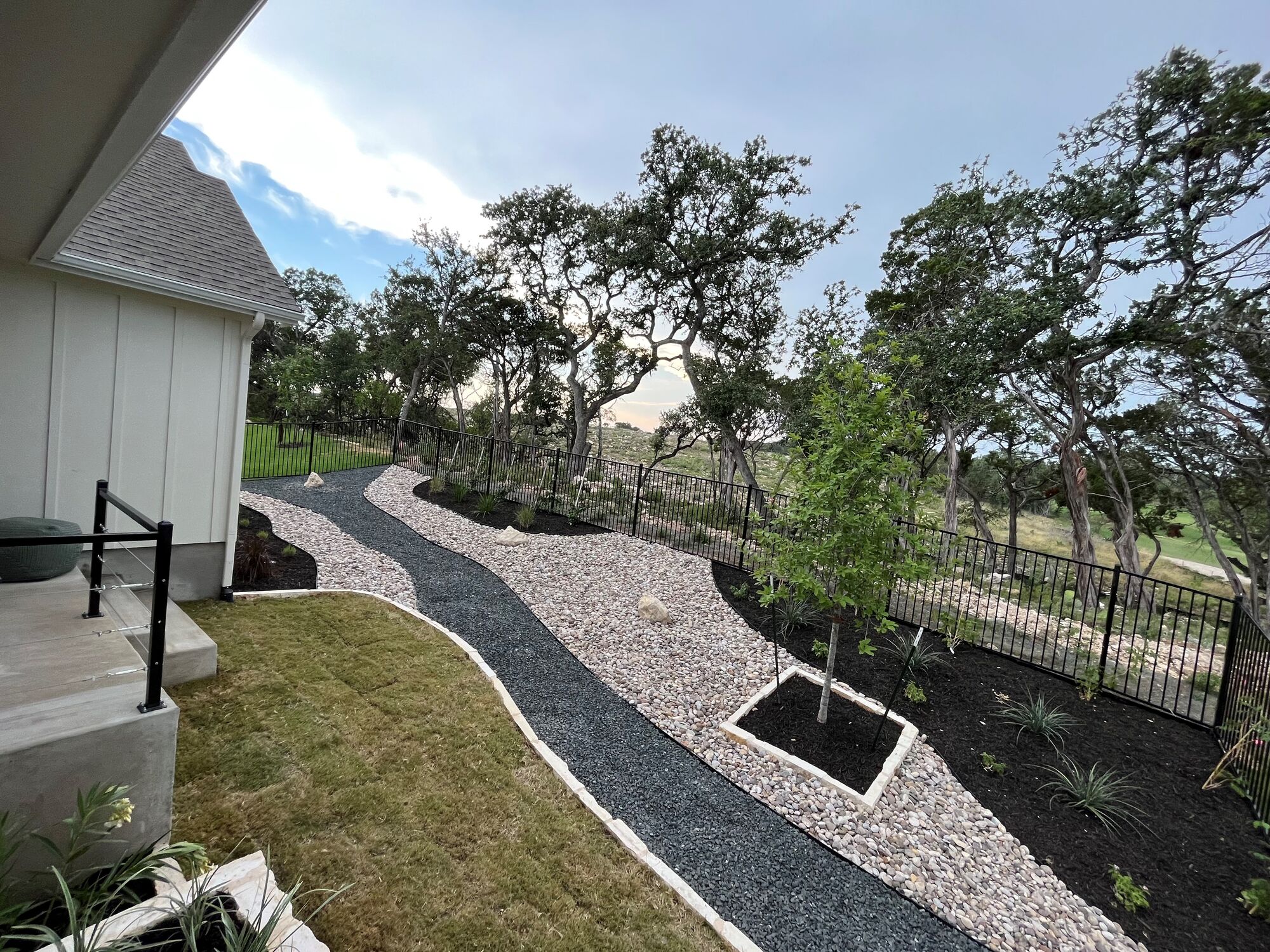 A finished Pioneer install: stone-edged gravel walkway and stone tree well with new plantings under mature oaks