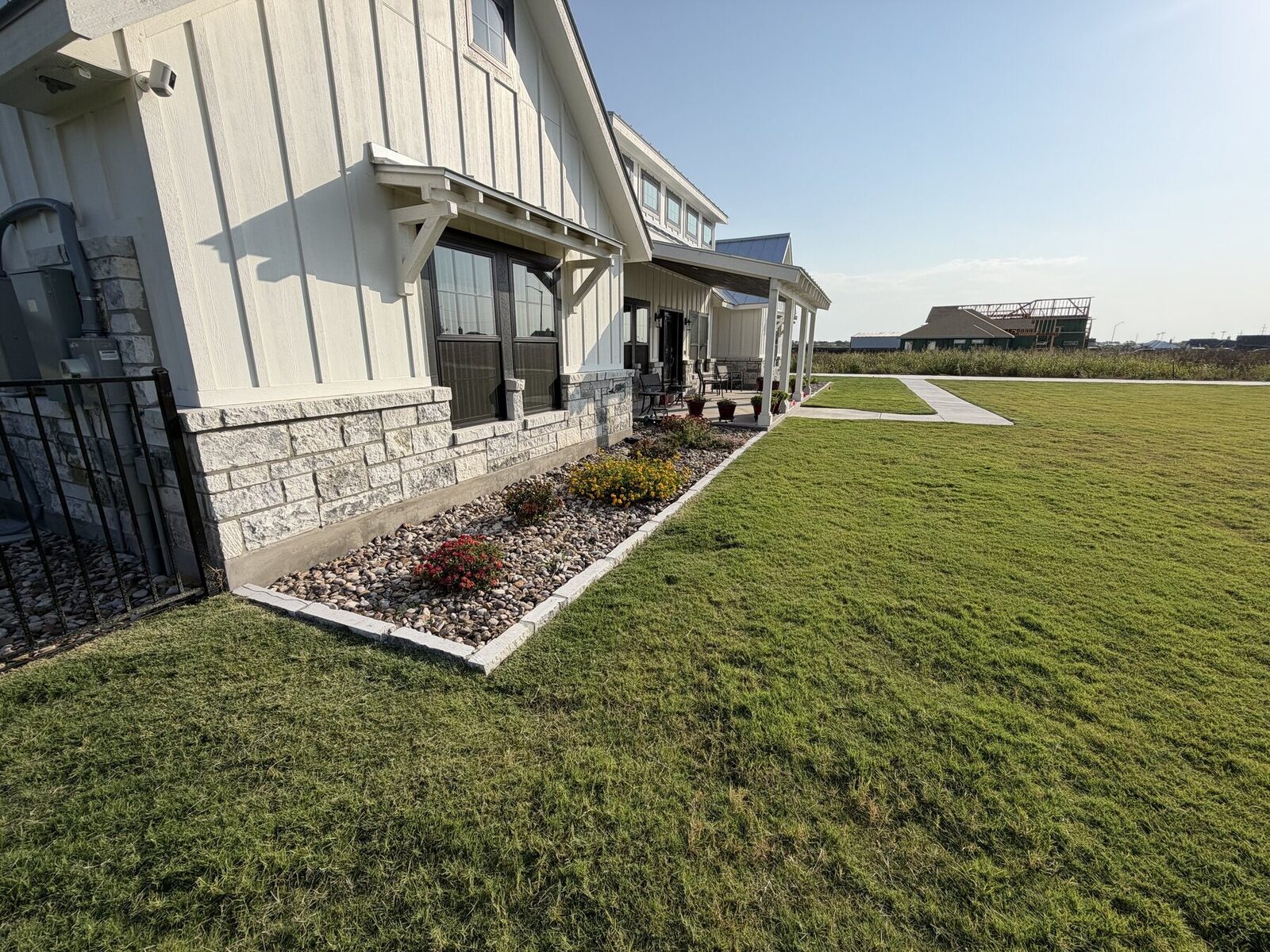 Close view of a limestone-edged bed with river rock and flowering perennials against limestone veneer and board-and-batten siding