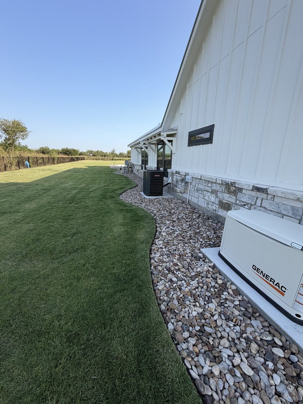 A steel-edged river rock bed running the side foundation line and curving around the air conditioning unit and generator