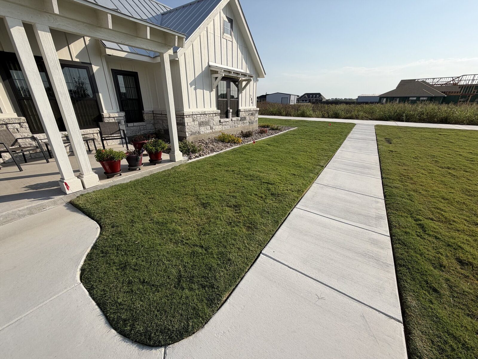 A curved sod panel between the covered porch and the concrete walk, with planted beds along the house
