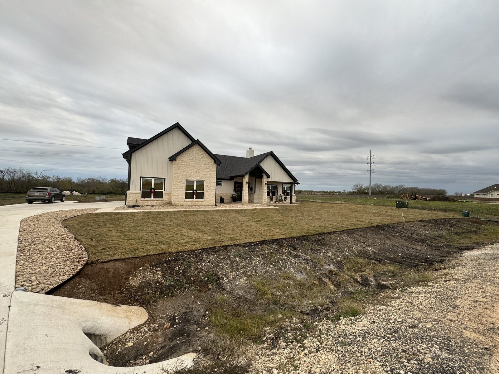A new sod apron cut to a curve against raw graded ground, with a river rock bed running alongside a concrete drive