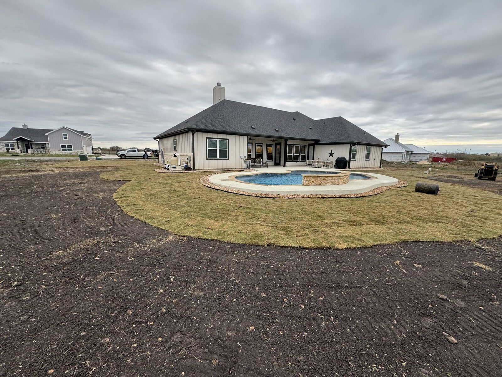 The back of the home with a pool, a raised stone spa, and a stone-bordered rock apron with sod laid around the deck