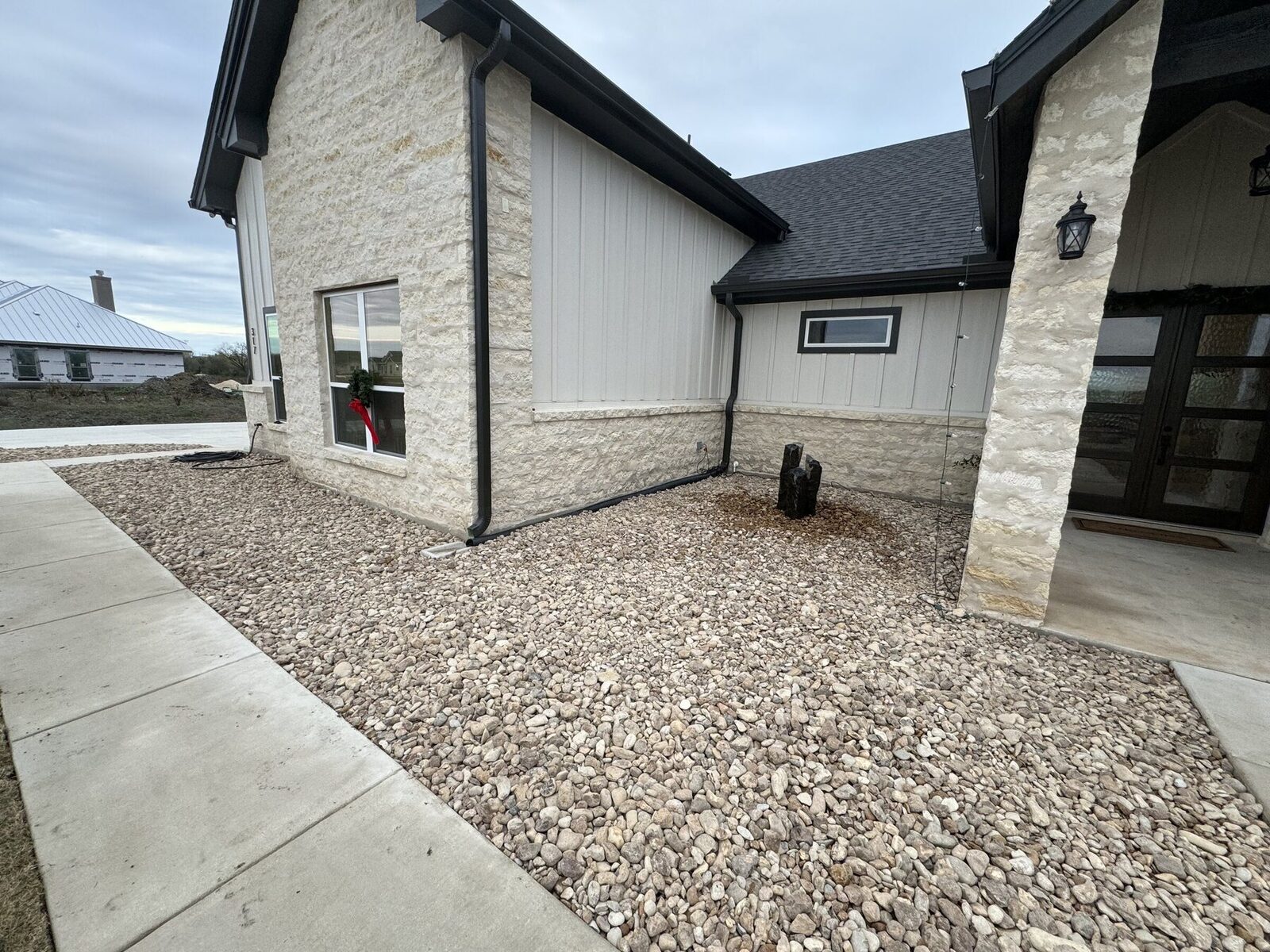 A stone entry courtyard filled with river rock and a dark basalt column water feature set beside the front door of a new limestone home