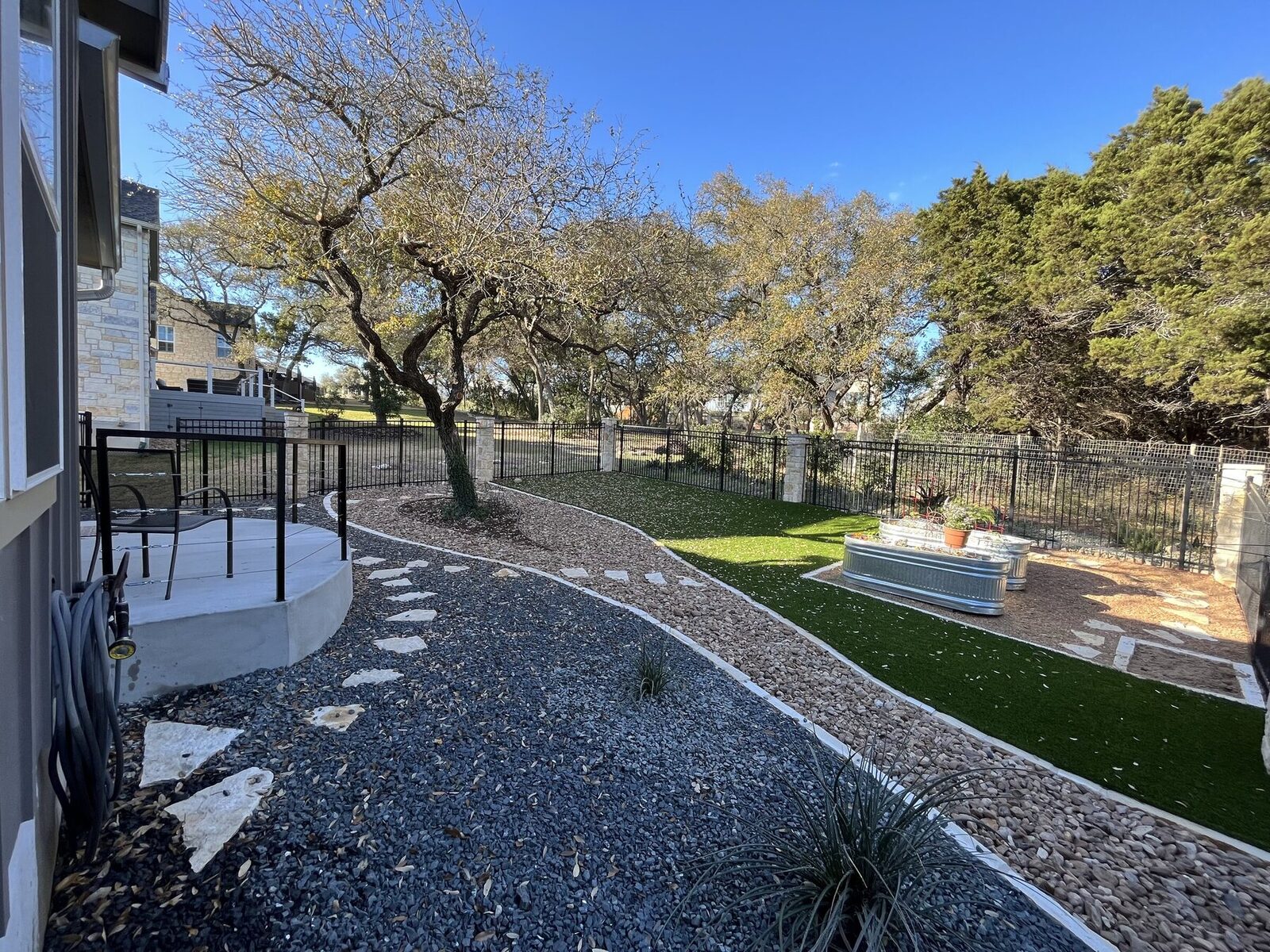 Wide view of the finished back yard with gravel beds, flagstone steppers, ornamental grasses, and a stock tank planter