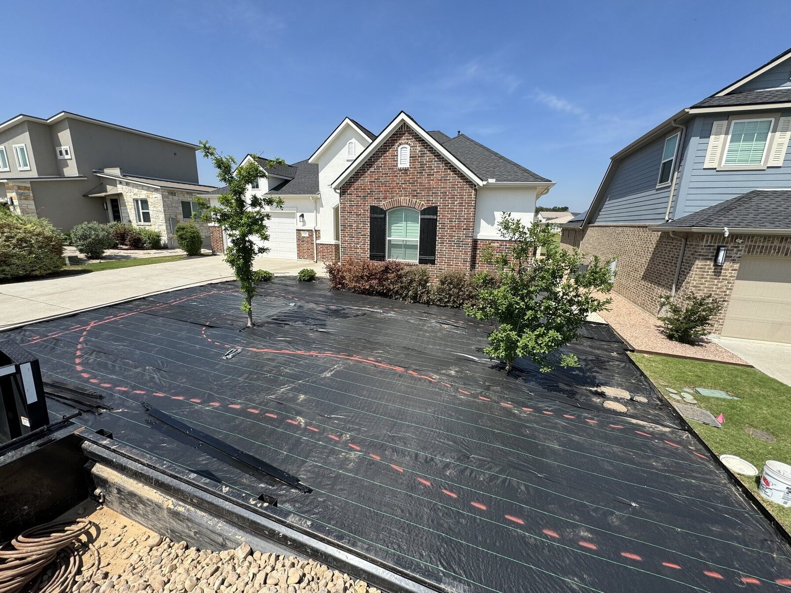 The same front yard mid build: weed barrier laid across the whole yard with the bed layout marked out in paint and steel edging staked